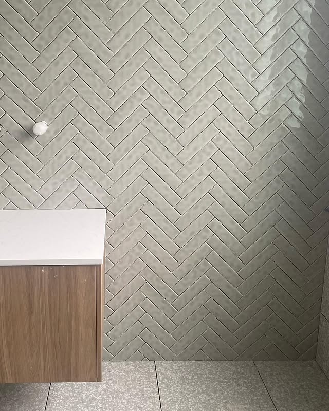 Sage green herringbone bathroom tiling with timber cabinetry