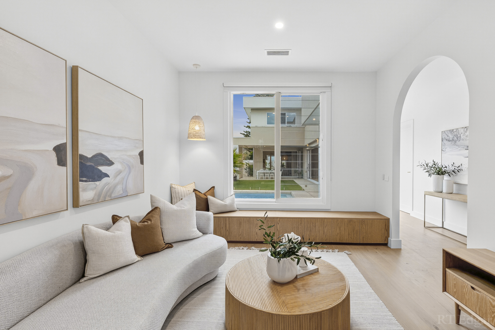 Curved sofa and round timber table in a bright sitting room overlooking the pool