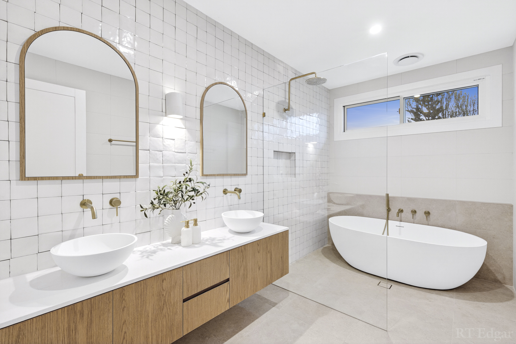 Bright bathroom with a timber double vanity, arched mirrors and freestanding bath